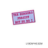 A pink embroidered letter patch with the text THE HORRORS PERSIST BUT SO DO I on a white background.