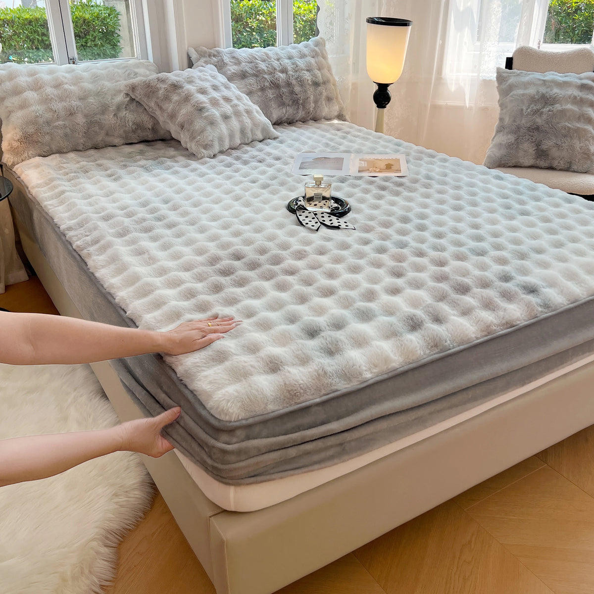 A luxury faux rabbit fur fitted sheet set displayed on a bed, with a hand touching the fabric.