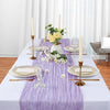 Lilac cheesecloth table runner with gold candlesticks and floral arrangements on a white tablecloth.