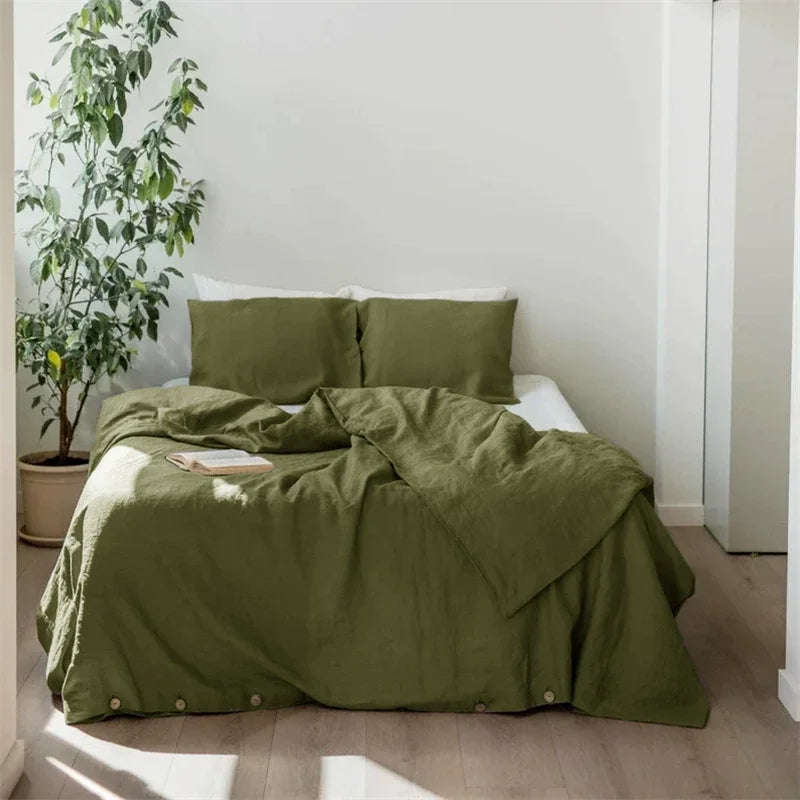 A luxury French linen duvet cover in olive green draped over a bed with white pillows and natural light.