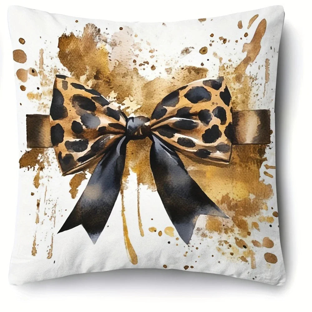 A decorative pillow cover featuring a black and gold leopard print bow on a white background with paint splatters.