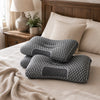 A gray ergonomic contour pillow is placed on a bed with a beige blanket and pillows.