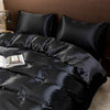 Black satin luxury bedding set with ruffled duvet and pillows on a bed.