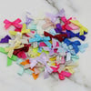 A collection of small satin ribbon bows in various pastel and bright colors scattered on a white marble surface.
