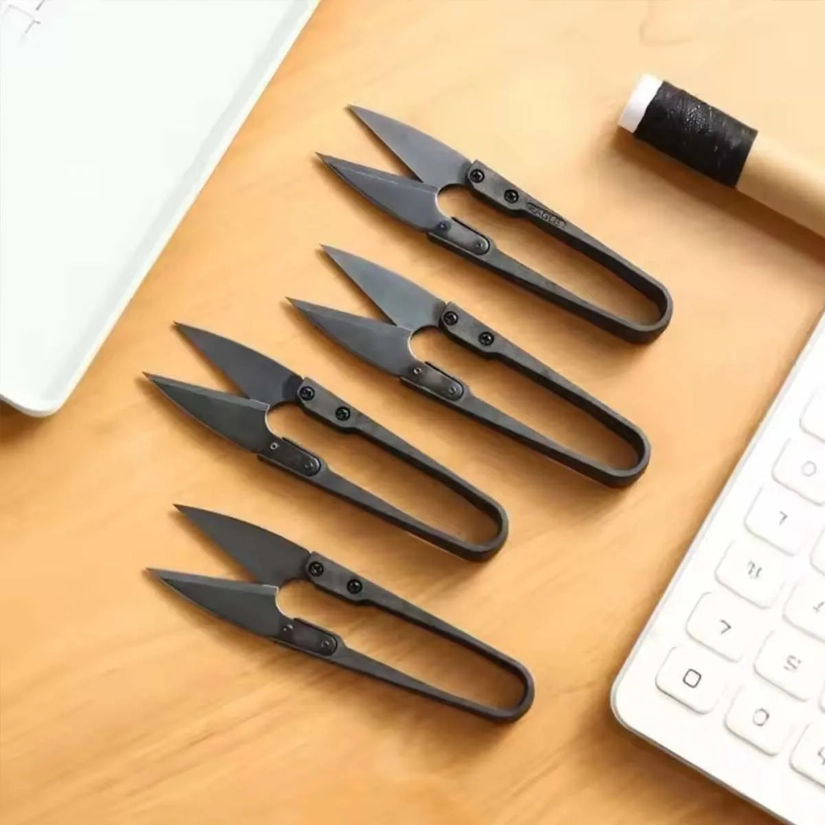 A set of black ergonomic stainless steel thread snip scissors resting on a wooden surface.