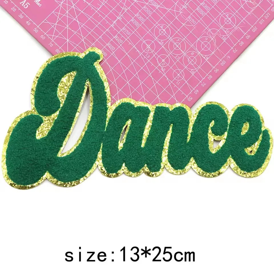 Green felt embroidered word Dance with gold glitter outline on a pink grid background