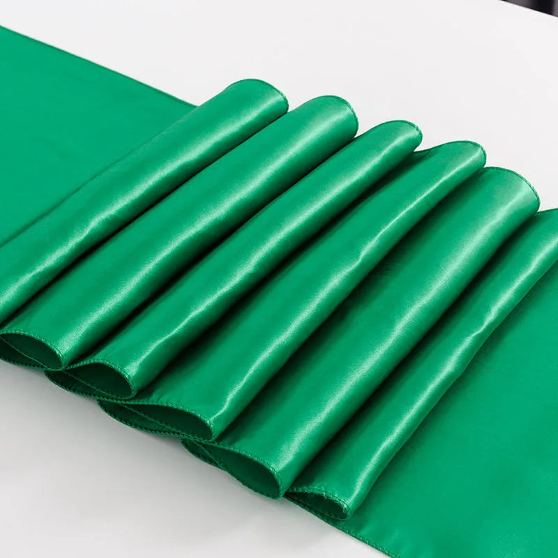 A stack of emerald green satin table runners laid out on a white surface.