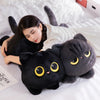 A black cat plush pillow is being held by a person lying in white bedding.