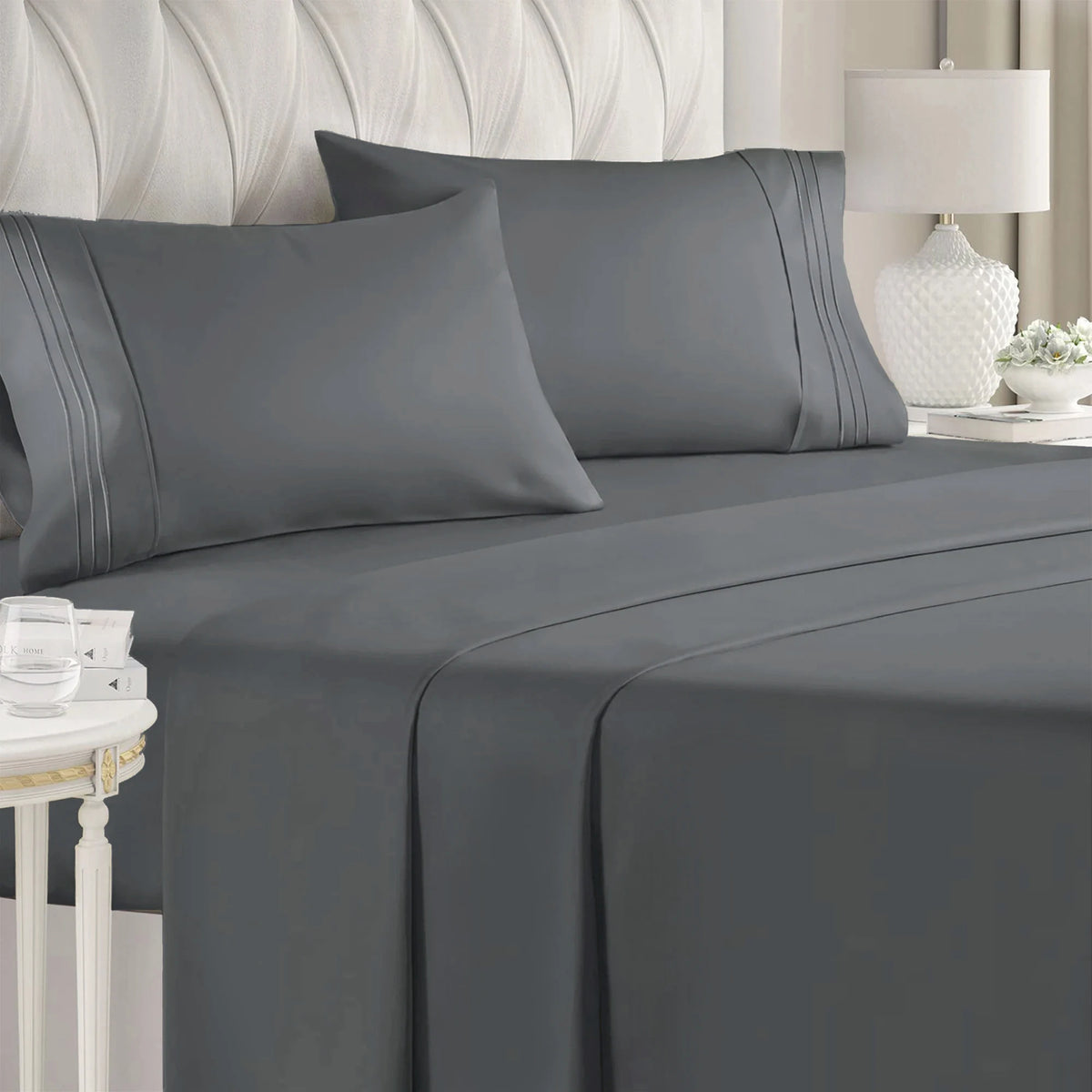 A gray luxury microfiber 4-piece bed sheet set with deep pockets is displayed on a bed with a white upholstered headboard.