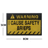 A rectangular yellow warning patch with black text that reads WARNING I CAUSE SAFETY BRIEFS