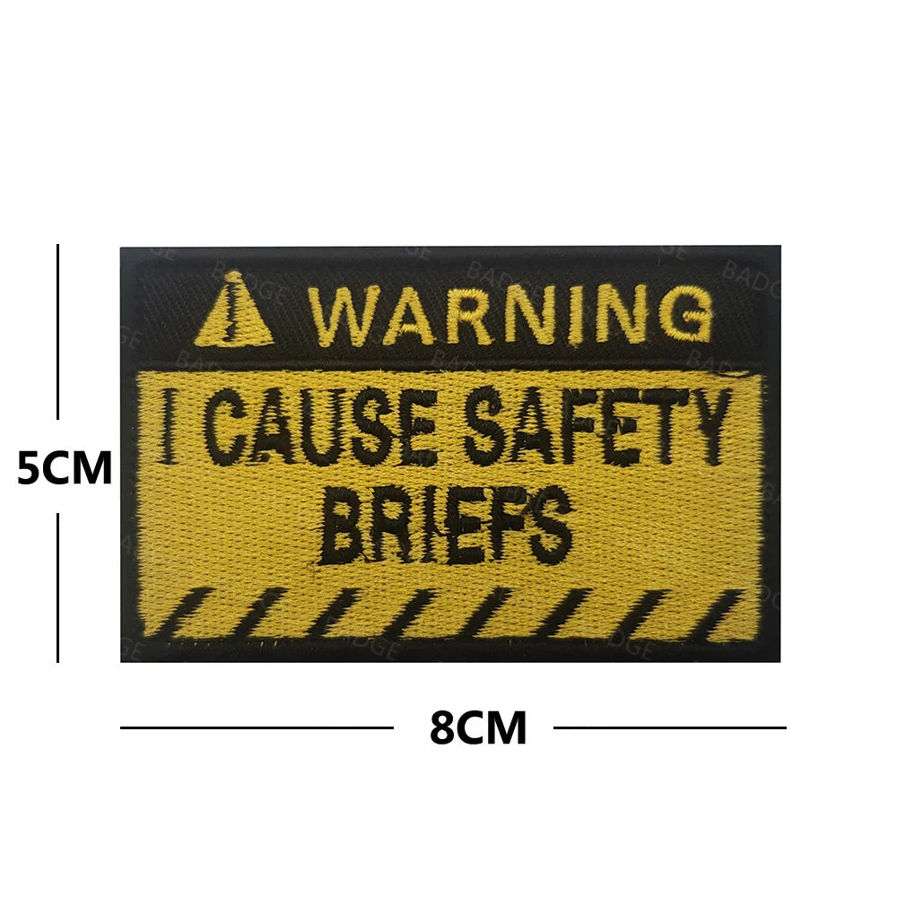 A rectangular yellow warning patch with black text that reads WARNING I CAUSE SAFETY BRIEFS