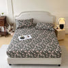 A floral printed cotton fitted sheet on a bed with a light upholstered headboard and bedside lamp.