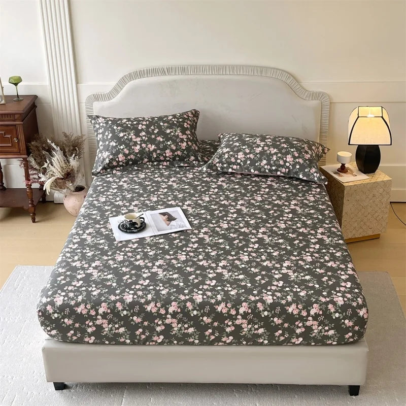 A floral printed cotton fitted sheet on a bed with a light upholstered headboard and bedside lamp.