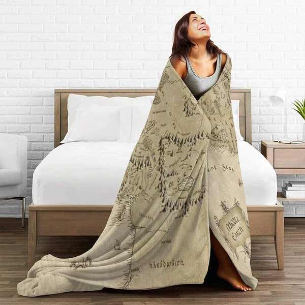 A woman wearing a beige Lord of the Rings themed blanket is smiling while lying on a bed.