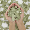 A pair of hands holds a green satin ribbon twist tie bow against a background of loose green ribbons.