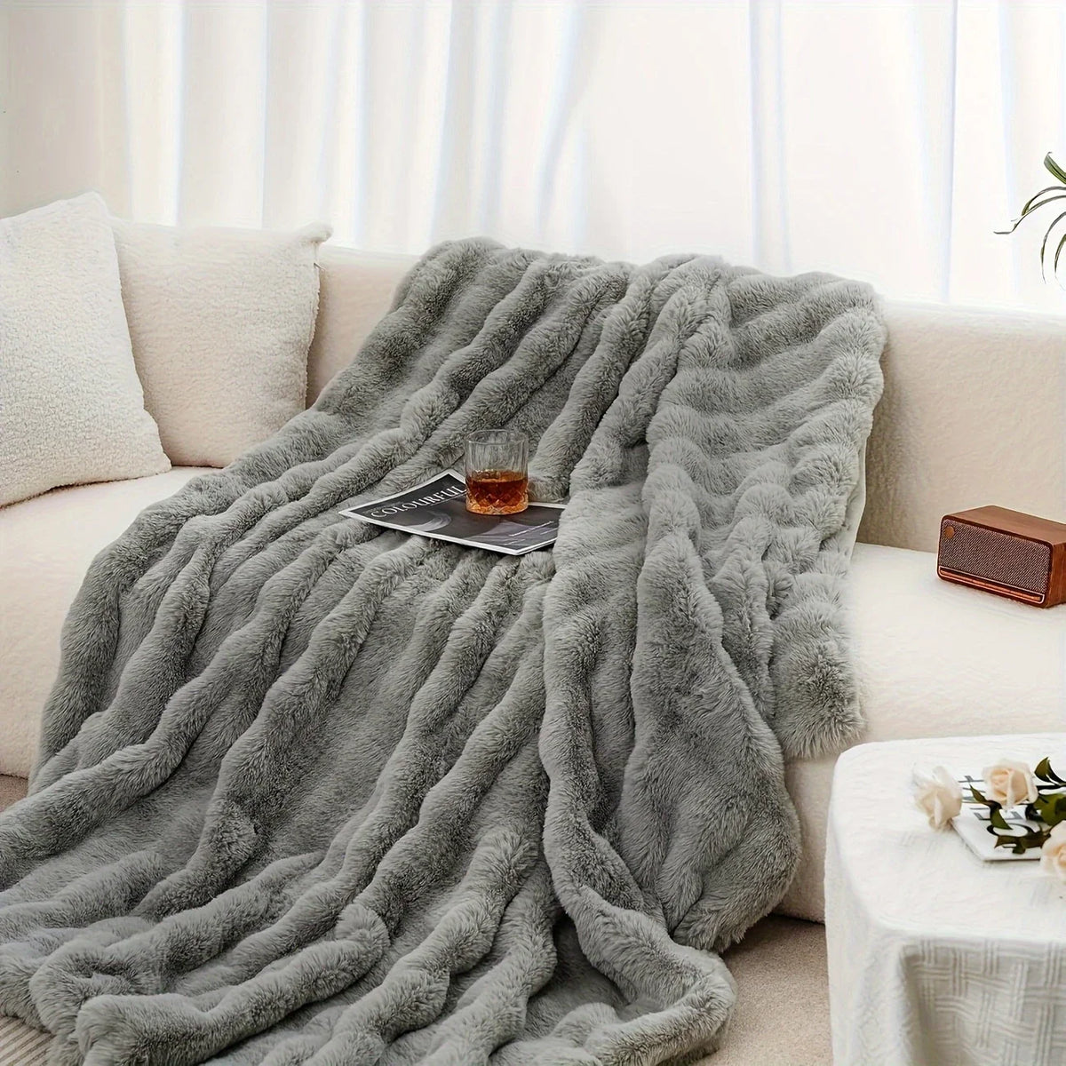 A gray plush faux rabbit fur throw blanket draped over a light-colored sofa.