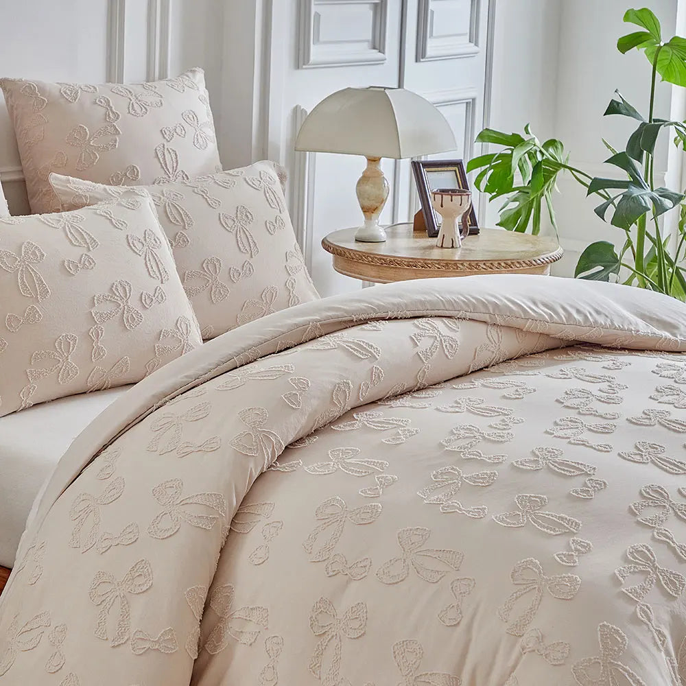 A beige luxury quilt duvet set with embroidered floral patterns on a bed, next to a lamp and green plants.
