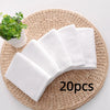 A stack of ten white cotton face towels resting on a woven mat next to a small potted plant.