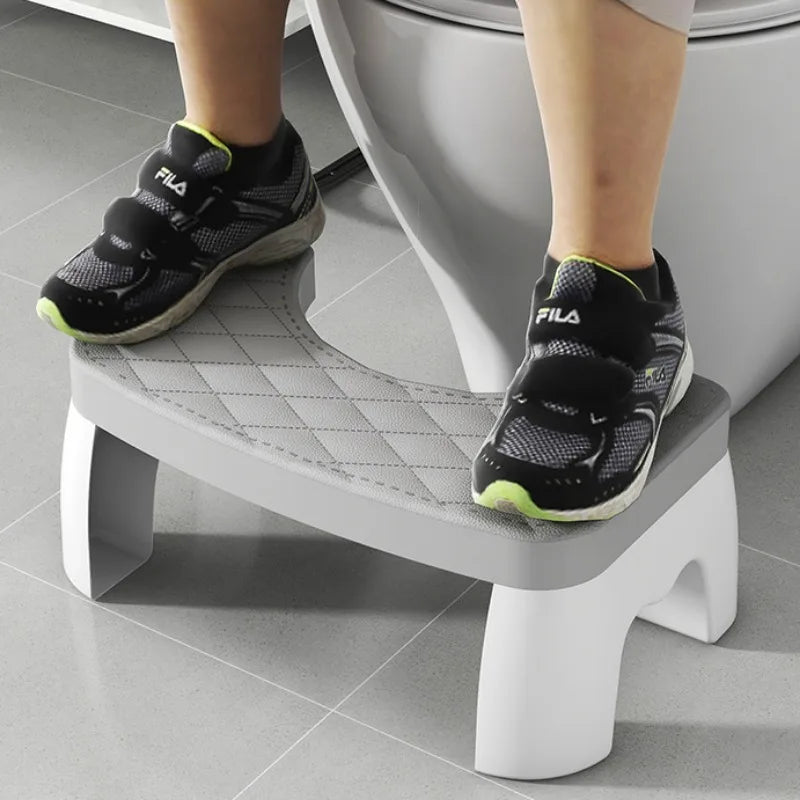 A pair of black and neon green FILA athletic shoes resting on a white adjustable toilet squat stool.