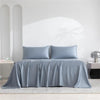 A light blue luxury organic bamboo bed sheet set draped on a bed with white walls and natural light.