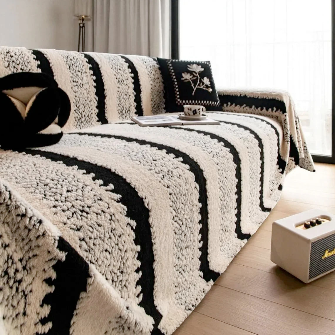 A close-up of a bohemian striped sofa cover featuring black and white fuzzy stripes on a light wooden floor.