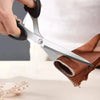 A hand is holding professional heavy duty fabric scissors with silver blades, positioned near a piece of brown fabric and a m