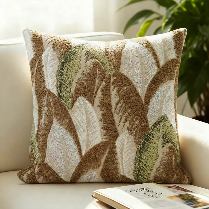 A textured, bohemian knit pillow cover in shades of brown and olive green rests on a light-colored sofa.