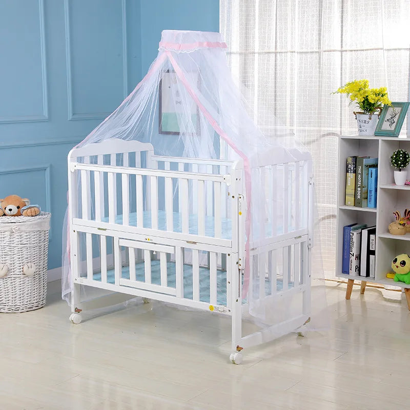 A white foldable baby crib with a sheer pink mosquito net canopy set up in a room.