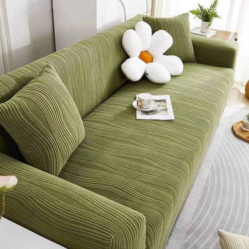 A green stretchable sofa cover with white decorative pillows and a cup on the seat.