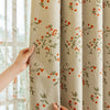 A close-up of beige blackout printed curtains with green leaves and orange berries hanging next to a window.