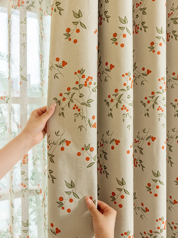 A close-up of beige blackout printed curtains with green leaves and orange berries hanging next to a window.