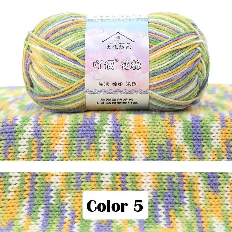 A ball of multicolored 4-ply cotton knit yarn with a gradient pattern resting on a colorful knitted fabric background.