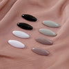 Eight plastic safety pins in black and white shades are displayed on a pink fabric.