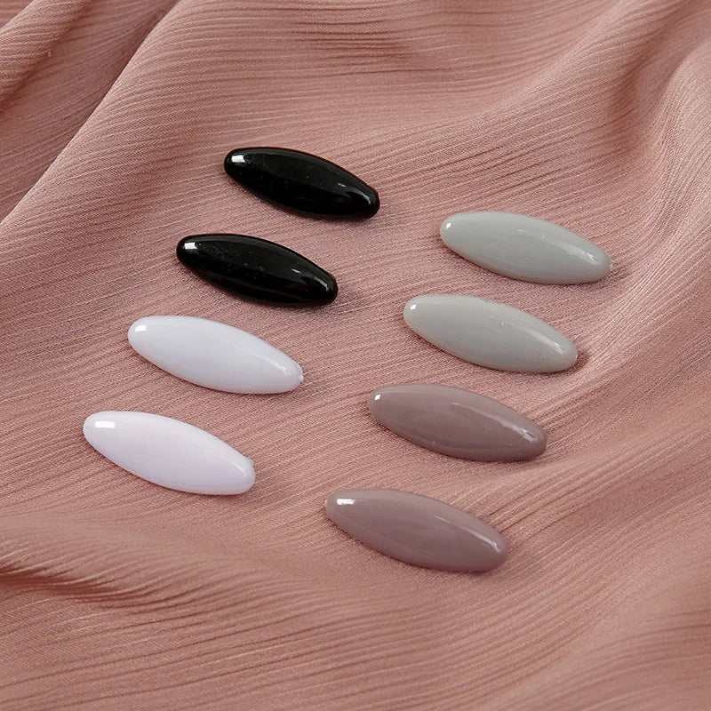 Eight plastic safety pins in black and white shades are displayed on a pink fabric.