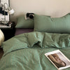 A close-up of a green and white striped duvet cover set on a bed with pillows and a lamp.