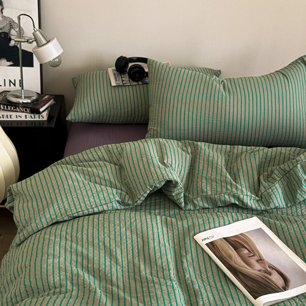 A close-up of a green and white striped duvet cover set on a bed with pillows and a lamp.