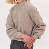 A close-up of a beige knitted sweater with a high neck and voluminous sleeves, worn by a person.