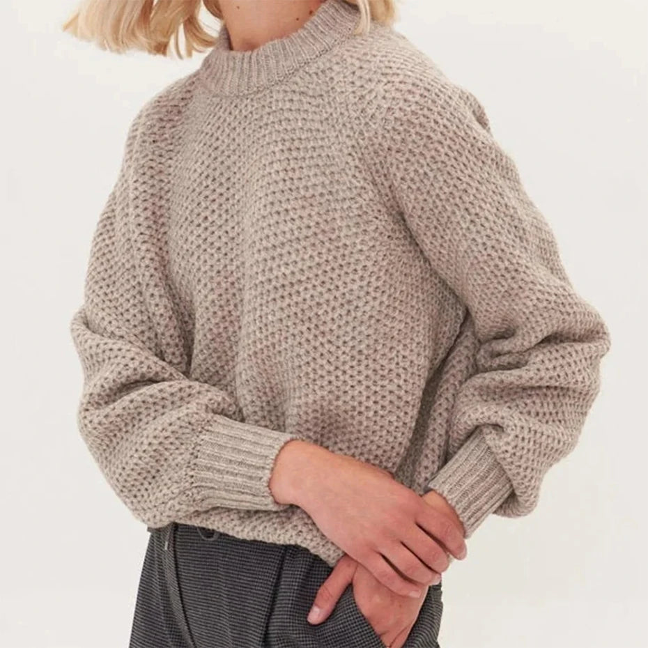 A close-up of a beige knitted sweater with a high neck and voluminous sleeves, worn by a person.