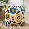 A white throw pillow cover with embroidered floral patterns in shades of yellow, blue, and brown.