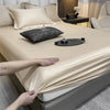 A close-up of a luxury Egyptian cotton fitted bed sheet being adjusted on a beige bed.