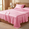 Pink striped satin bedding set displayed on a wooden bed with a headboard and bedside lamp.