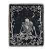 A black throw blanket featuring a white line art design of a skull, branches, and a crescent moon.