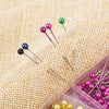 A collection of colorful pearl head sewing pins in various shades are displayed on a burlap fabric.