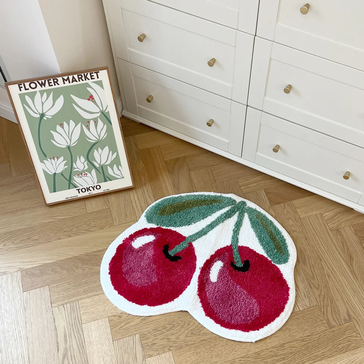 A blush pink soft tufted area rug shaped like a green apple with red leaves on a light wood floor.