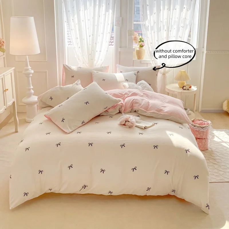 A white duvet cover with a subtle black bowknot embroidery is displayed on a bed, surrounded by pink bedding and decor.