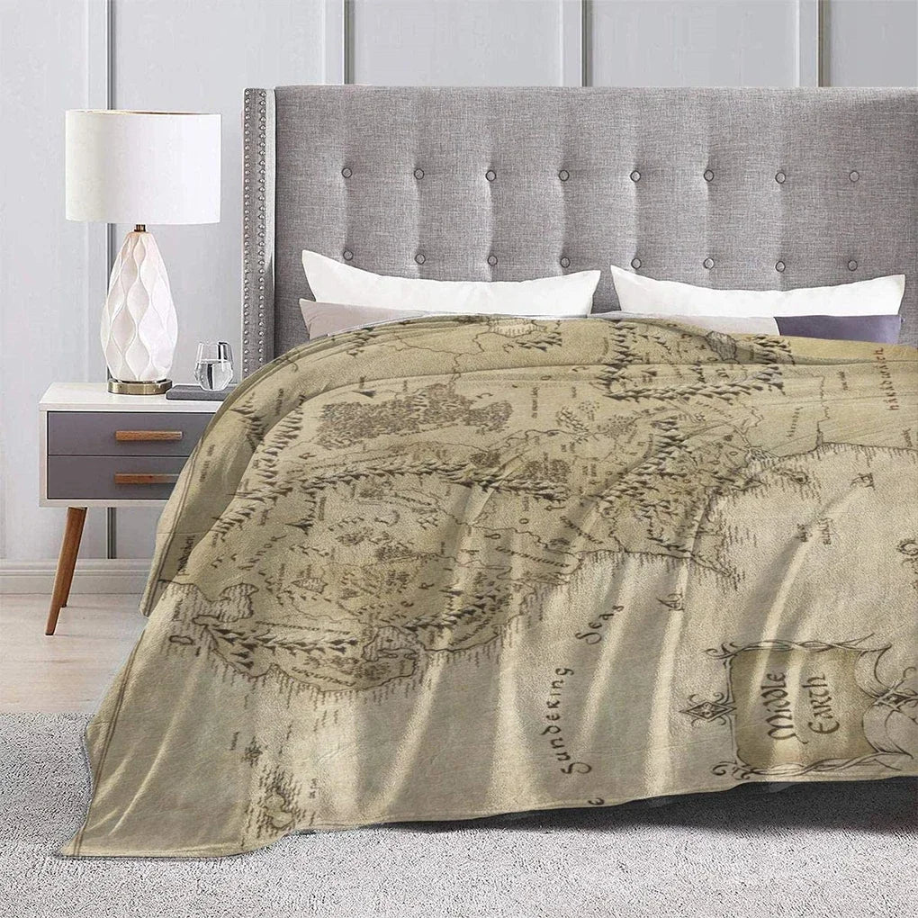 A beige blanket featuring a faded map design for a bed, set against a gray upholstered headboard.