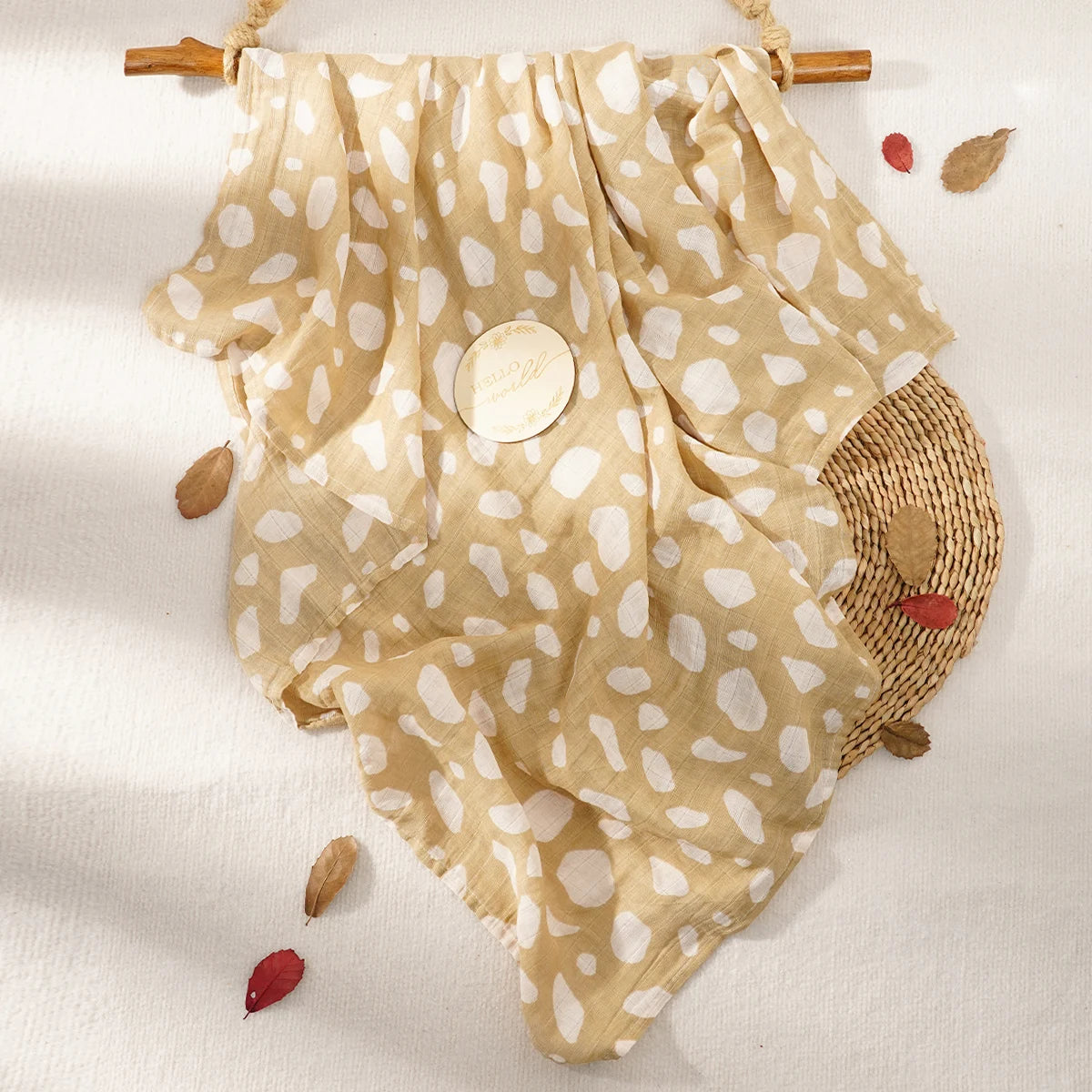 A beige muslin swaddle blanket with white polka dots is displayed on a light background.