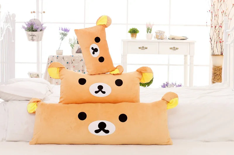 An orange Rilakkuma plush bed pillow and sofa cushion resting on a white bed with white linens.