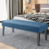 A rectangular blue velvet bench slipcover with gray legs placed on a striped rug in a bedroom setting.