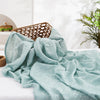 Light mint green muslin swaddle blanket draped on a white surface with a woven basket in the background.